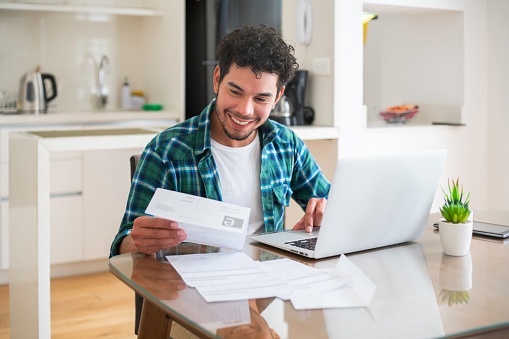 Happy Latin American man paying his utility bills online from home - home finances concepts