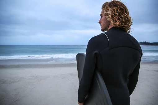 Young man at the beach with surfboard in a wetsuit
