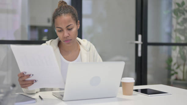 istock African Woman with Laptop Reading Documents in Office 1421143292