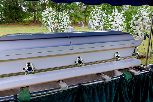 A funeral service is held in a cemetery followed by the coffin being lowered into grave by an automatic elevator before burial