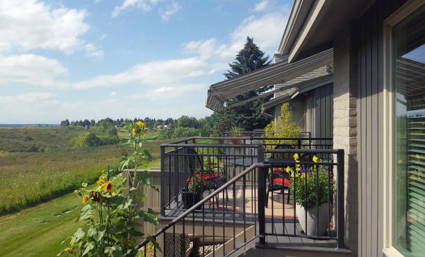 Back of house with deck. Summer. Awning. Outdoor furniture,Sunflowers,Snap Dragons, Straw Flowers and iron railings. Field and green hills in background.