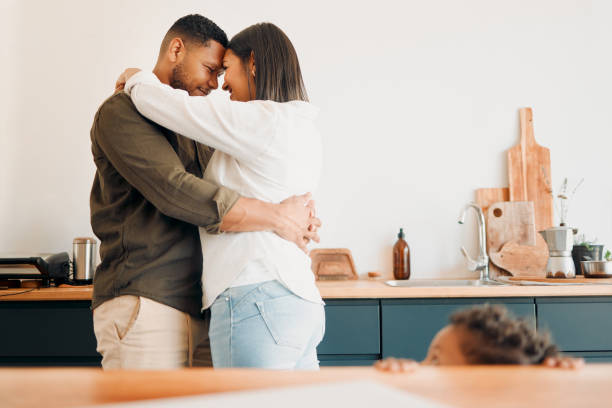 istock Cosy couple hugging, romance and affection in a modern kitchen with small child looking at them. Loving, young and parents, mom and dad embrace, excited by the future of their growing family 1421148561