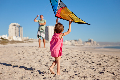 Little girl learning to play with a kite on the beach