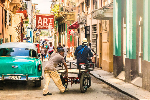 Havana, Cuba - July 18 2018 : Carts, people and vintage cars with an art sign above the street in the old town