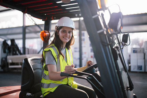 Portrait of a young woman driving a forklift in construction warehouse.