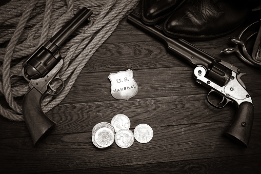 Old western revolver guns with U.S. Marshal badge and silver dollars with hat, rope and cowboy boots