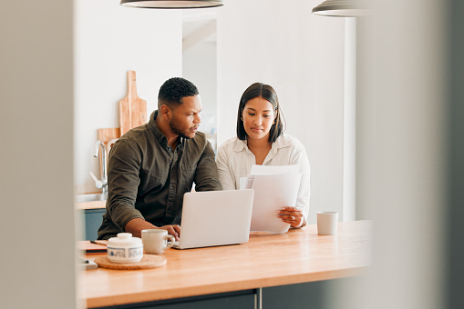 Couple with laptop looking at document, paper work or finances with confused expression for overdue expenses, budget or mortgage home loan. Married man and woman managing utility bills or debt online