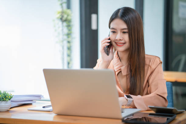 istock Asian businesswoman talking on mobile phone in front of a laptop computer at office 1421159607