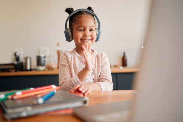 istock Distance learning, education and virtual student child on a video call lesson with a headset and laptop doing hello or bye greeting gesture. Little girl in an online classroom, homeschooling at home 1421162252