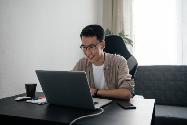 istock Middle aged happy asian man working at home with laptop. 1421164429