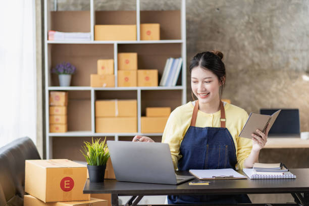 mujer asiática trabajando en casa con caja amarilla y computadora portátil para tomar pedidos, ideas de negocios de pymes sobre entrega de paquetes - smiling business card horizontal women fotografías e imágenes de stock