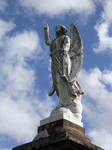 Old statue of an angel pointing towards the sky with clouds