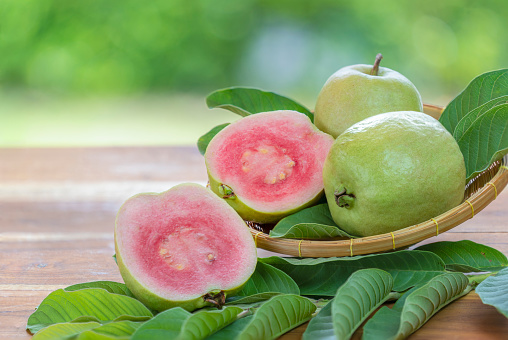 Red Guava fruit with leaf on blur garden background, Fresh Pink Guava fruit on wooden basket over natural farm background.