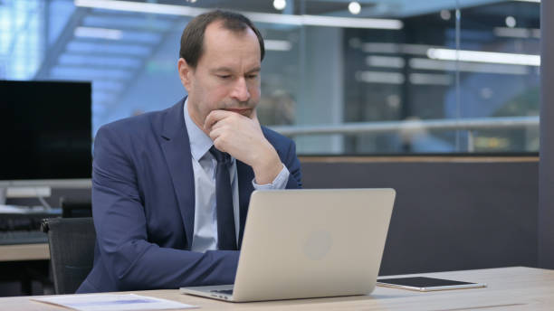 istock Businessman Thinking while Working on Laptop in Office 1421184847