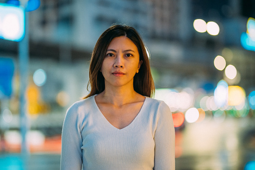 Closed-up image of An Asian Chinese businesswoman look at camera in downtown city street at night