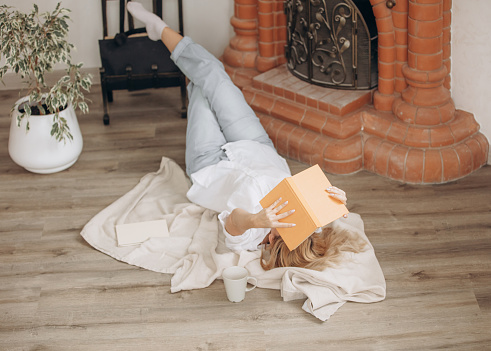 Young adult woman is reading a book on the floor in the interior.