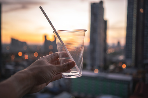 Human hand raised and holding up iced drink to the sky against urban city skyline
