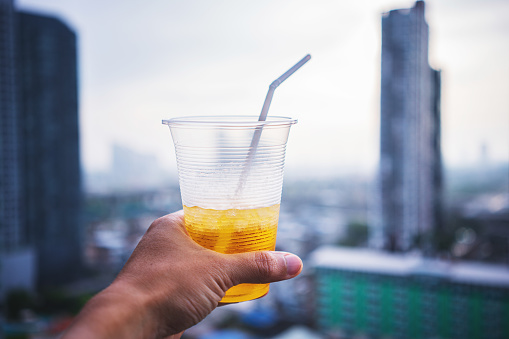 Human hand raised and holding up iced drink to the sky against urban city skyline