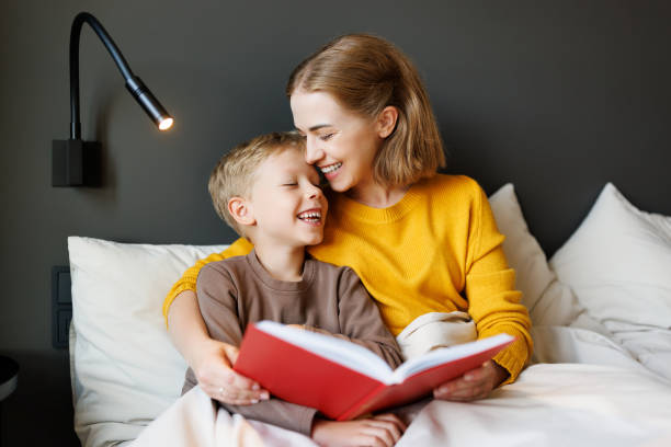 istock Happy mother and son reading book together on bed 1421196112
