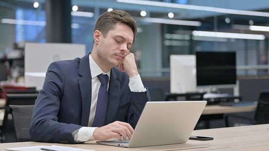 Tired Young Businessman taking Nap While Sitting in Office with Laptop