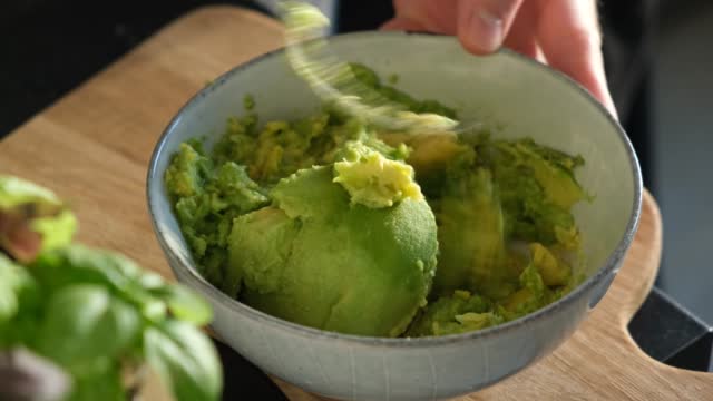 Preparing guacamole, mashing avocado with fork in bowl