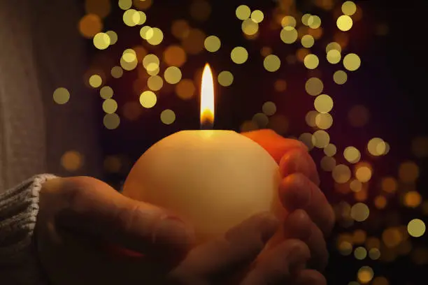 Photo of Closeup view of woman holding burning candle in darkness, bokeh effect. Christmas Eve