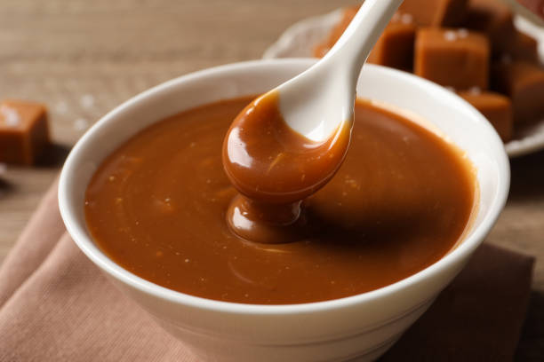 istock Taking yummy salted caramel with spoon from bowl at table, closeup 1421198852