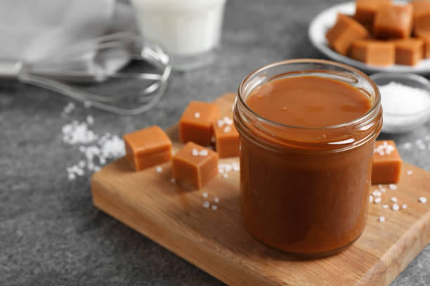 istock Yummy salted caramel in glass jar and candies on grey table, space for text 1421199045