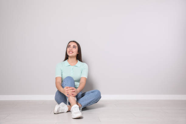 mujer joven sentada en el suelo cerca de una pared gris claro en el interior. espacio para texto - young women sitting simple living eastern europe fotografías e imágenes de stock