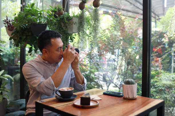 A matured Asian man using a vintage camera taking photo at a garden cafe