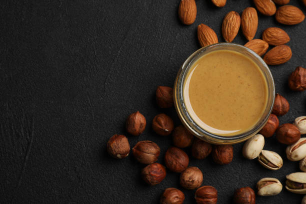 istock Delicious hazelnut butter and different nuts on black table, flat lay. Space for text 1421202392