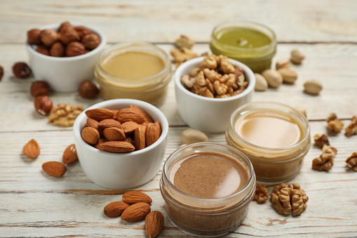 Jars with butters made of different nuts and ingredients on white wooden table, closeup