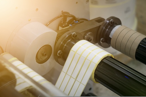 A machine for the production of white self-adhesive labels. The shafts of the machine for winding rolls of tape with a label. Die-cutting and cutting of paper for label production. Selective focus
