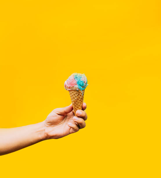 istock Hand holding ice cream cone on yellow background. Hand holding a waffle cone ice cream isolated. Waffle cone ice cream concept on yellow background 1421206755