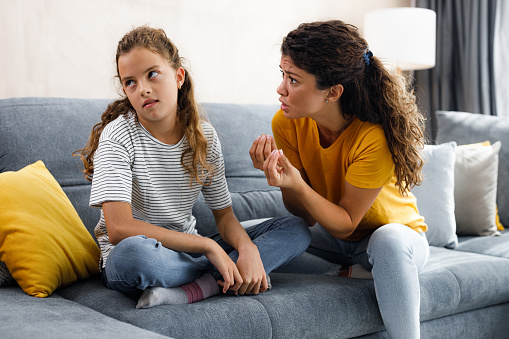 Frustrated single mother talking to her rude girl who is ignoring her at home.