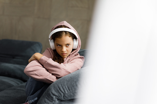 Angry little girl listening music over headphone while ignoring her life at home. Copy space.