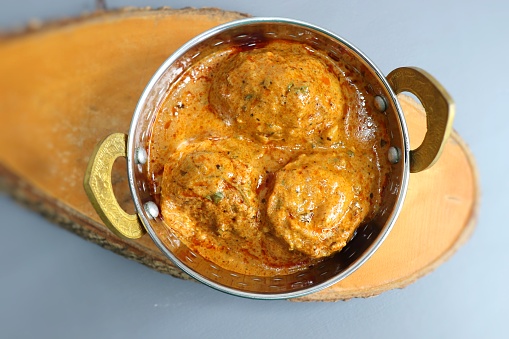 Indian cuisine- Paneer Stuffed dum aloo. Kashmiri Dum Aloo or Potatoes in red gravy over white background. Paneer Bharwa alu. Garnished with coriander. Copy space. Panjabi Dam alu curry.