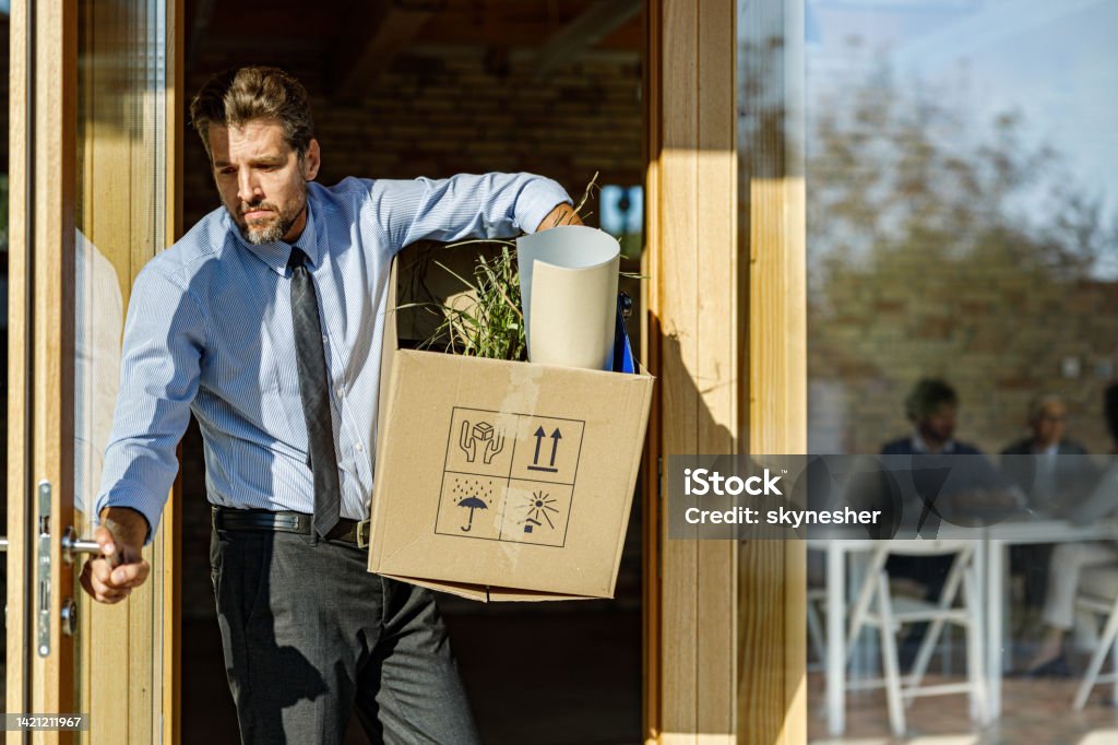 Depressed businessman leaving the office after being fired from his job. Sad businessman leaving the office with his belongings after being fired from his job. Quitting a Job Stock Photo
