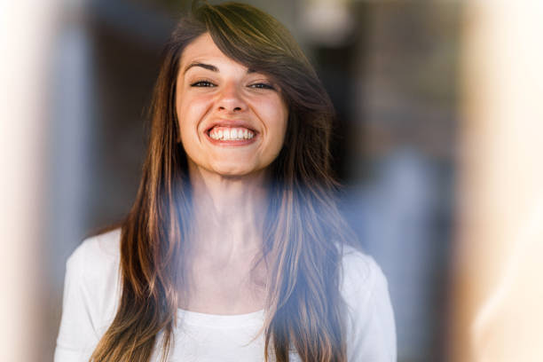 Portrait of young happy woman with toothy smile looking at camera. The view is through glass.