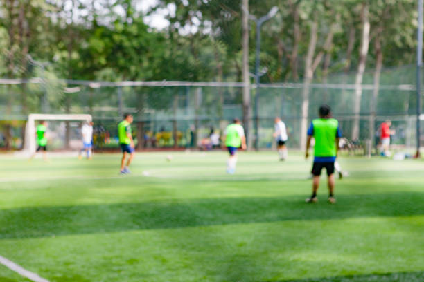 des gens qui tapent dans le ballon sur le terrain de soccer dans le parc, hors de propos - american football football focus on foreground team sport photos et images de collection