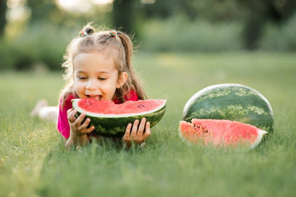 istock Cute baby girl with fruit melon on green grass 1421215510