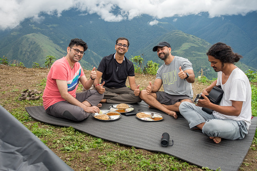 March 13th 2021 Nag Tibba Mountain, Uttarakhand India. A group of campers and hikers enjoying meal and playing guitar at the base camp site.