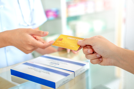 Young asian pharmacist receive credit card  payment pharmacy  on the customer's  settle medical expenses