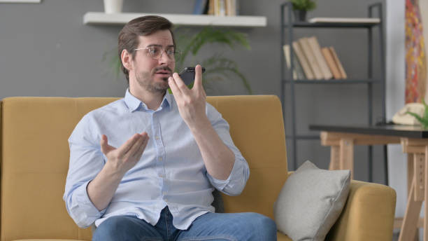 istock Angry Young Man Talking on Smartphone on Sofa 1421218699