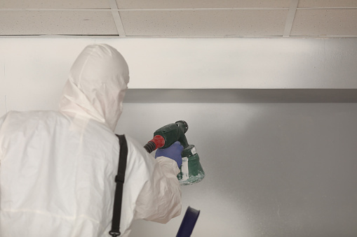 Worker paints wall white with spray gun. Painter in protective suit with spray gun concept
