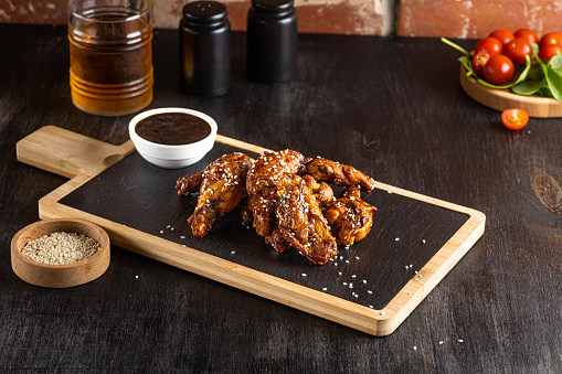 Grilled teriyaki chicken wings with sesame on dark cutting board on dark wooden background