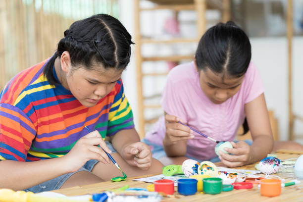 istock Children painting eggs with brush in class workshop. Two girl sculpts  modeling clay multi-colored plasticine in class of school. craft and clay art and education concept 1421221637