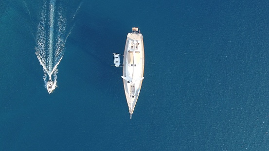 A aerial drone shot of a private yacht and small motorboat sailing on blue ocean on sunny day