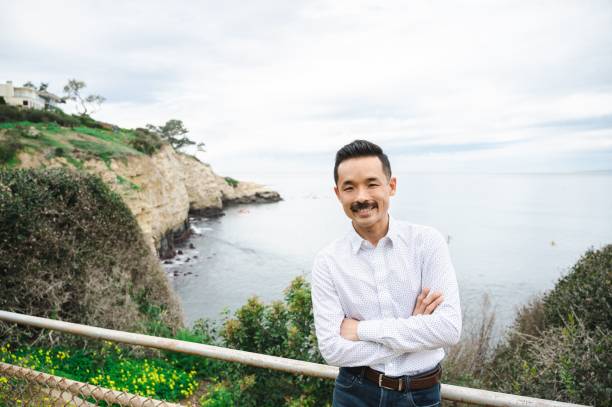 feliz empresario asiático japonés de pie en el fondo del mar en san diego - on top of business cliff businessman fotografías e imágenes de stock