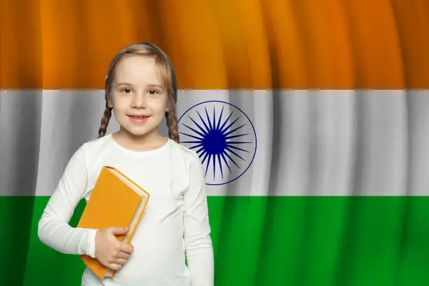 Photo of Beautiful small kid girl with book on flag of India background. Learn Hindi language concept.